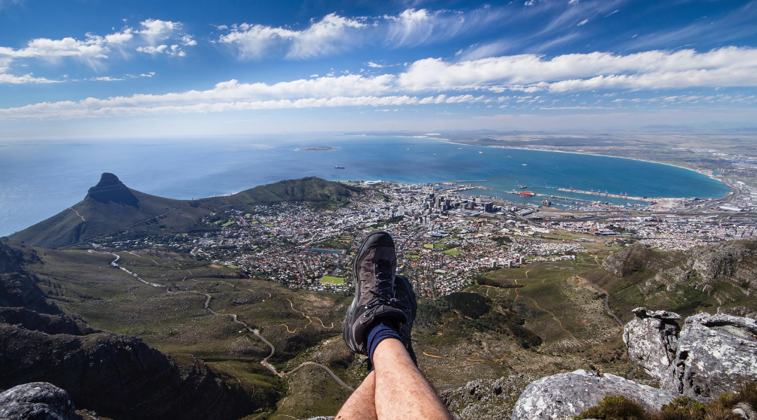 Vista panorâmica de Cape Town, África do Sul, a partir do topo de uma montanha, com os pés de uma pessoa em primeiro plano.